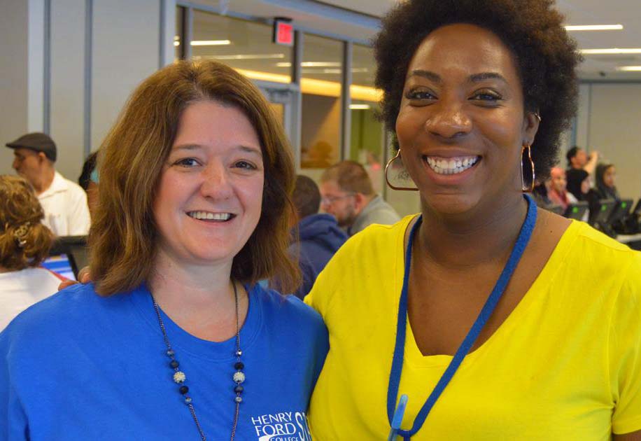 Henry Ford employees smiling in the Welcome Center with students enrolling or registering in the background