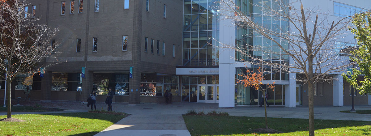 Health Sciences Education Center (Building G), shown during the fall, accompanied by students walking, sitting, or standing and talking to each other