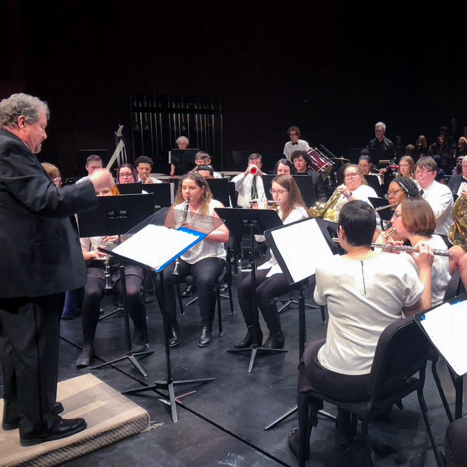 Close up of musicians in symphony band with conductor performing on stage