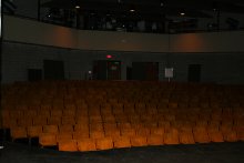 View of seats from an on-stage perspective, showing a top level where various theater equipment is used and maintained, and the sets of doors leading out of the auditorium on the main floor on the back wall, behind the seats