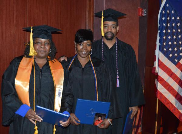 From left to right: Brenda McCall, Beverly Etchen and Carl Matsey II stand in graduation gowns and caps holding diplomas