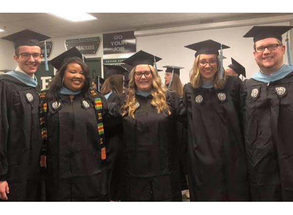 Photo of 5 employees (2 men, 3 women) in graduation attire