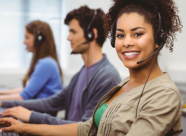 A smiling customer service representative with other customer service professionals in the background.