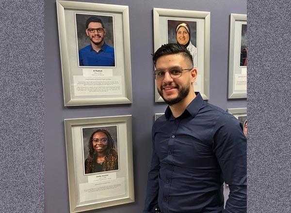 Photograph of HFEC alumnus standing before the Wall of Fame at HFEC.