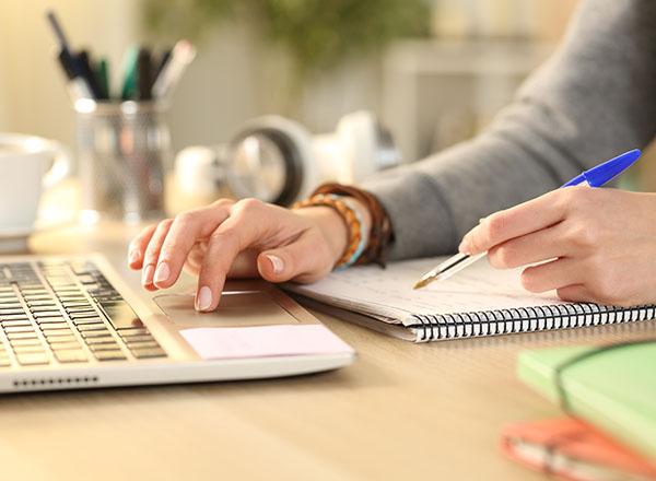 image of a person typing on a computer while writing in a notebook.
