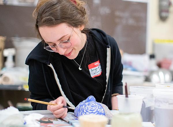 Photo of a female student putting the finishing touches on her artwork. 