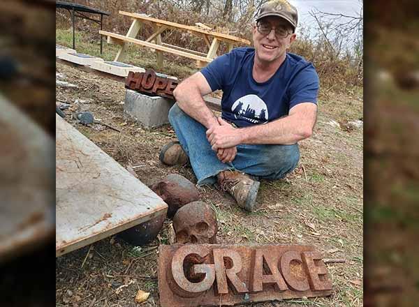 Jay Elias sitting on the ground with metal sculptures.