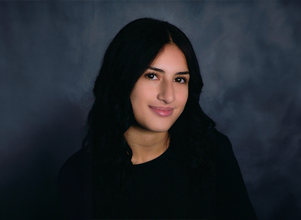 Alyssa Oudeh smiling with a dark blue background.