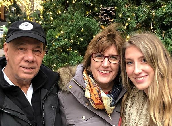 Al Burrell (left) and family smiling in front of a lit holiday tree. 