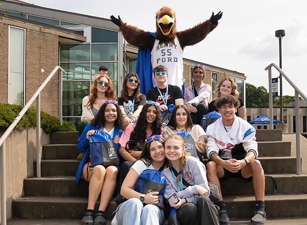 Students seated on stairs and the Hawkster's arms are held out.