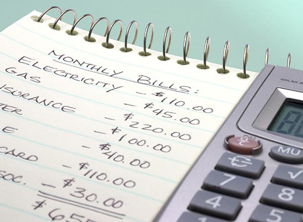 A pad of paper with monthly bills and a calculator.