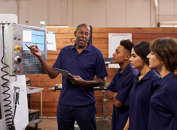 Engineer training apprentices on CNC machine.