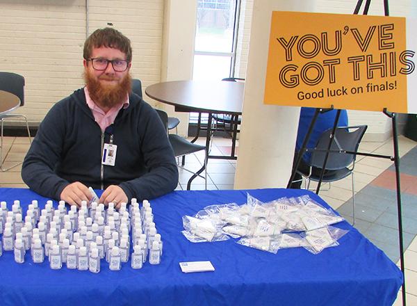 A person sitting behind a table with snacks and a sign that reads "You've Got This - Good luck on finals!"