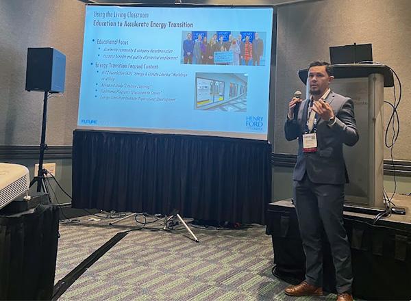 Nick Paseiro, wearing a grey suit and standing in front of a projection screen giving a presentation.