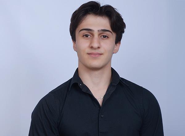 Hassan Berry wearing a black button-down shirt in front of a pale blue background.