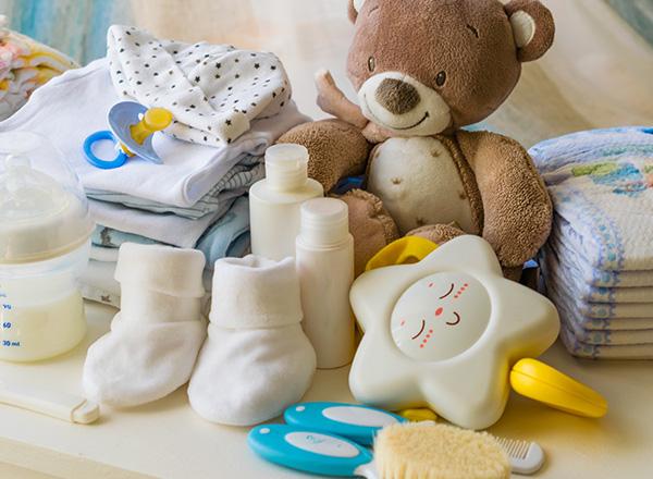 Baby accessories such as clothing, baby lotion, towels, baby bottles, baby brush, baby socks, diapers, rattle, teddy bear, laid out on a dresser. 