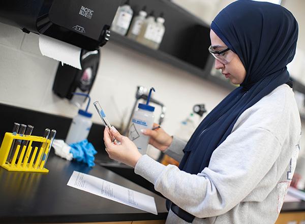 Science student examining test tube and making notes.
