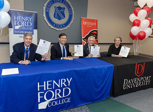 four people sitting behind tables, holding up documents