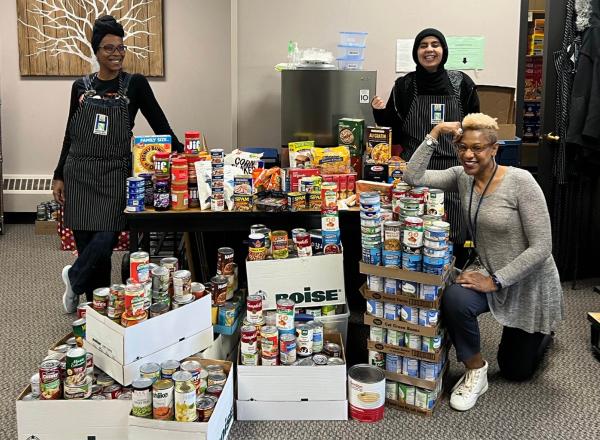 Rochelle Taylor and 2 students posing in front of the food donations. 