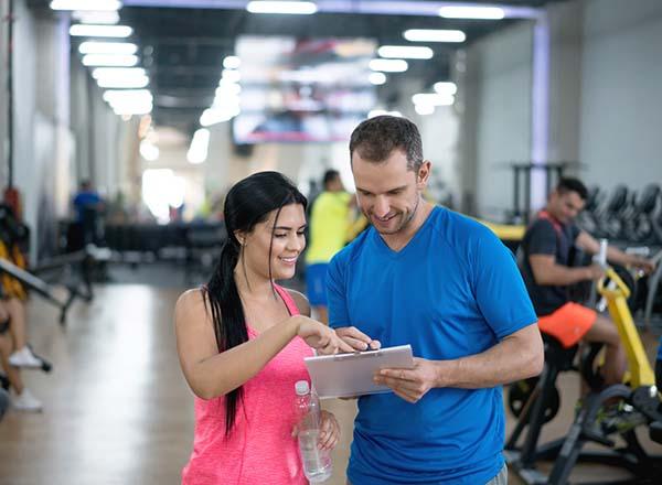 A male gym trainer showing a female information on a clipboard