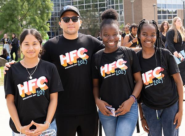 Four Discover Day volunteers posing outside, wearing the black 2023 Discover Day volunteer shirt styled like the vintage MTV logo. 
