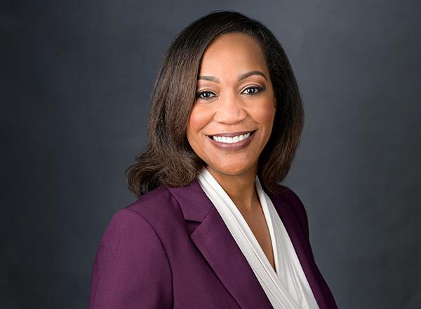Michele Shelton, smiling, has shoulder length brown hair and wearing a plum colored suit jacket with a white blouse. 