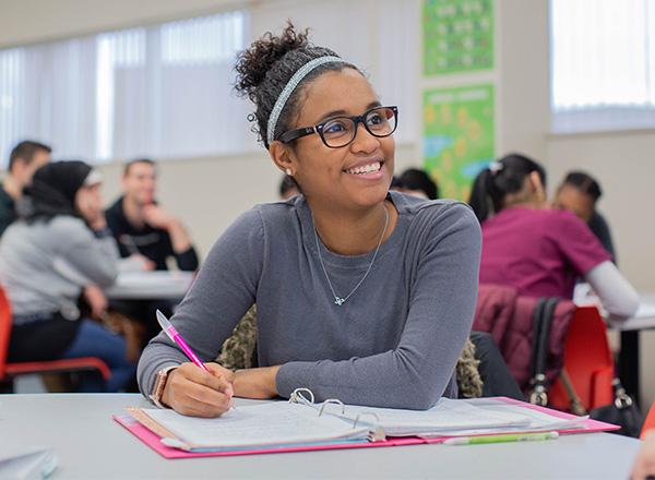 Female student smiling and taking notes in class.