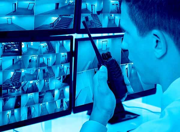 Image of dispatcher speaking on a walkie talkie and looking at a screen of video feeds.