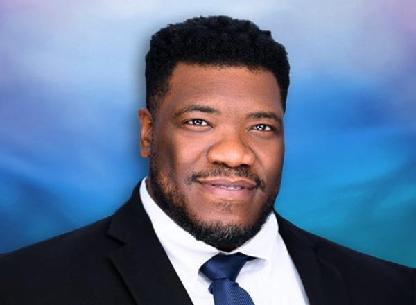Portrait of Mark Yancy, Jr., dressed in a suit with a blue background