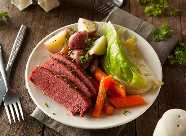 Homemade corned beef and cabbage with carrots and potatoes placed on a wooden table.