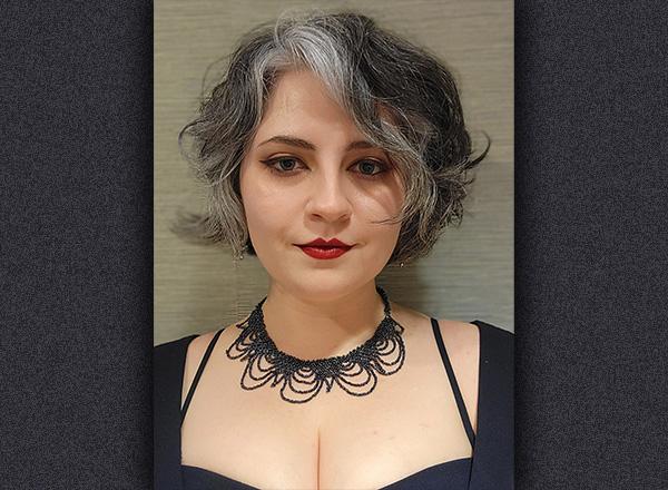 Headshot of Kate Warden with short hair wearing red lipstick and a black beaded necklace.