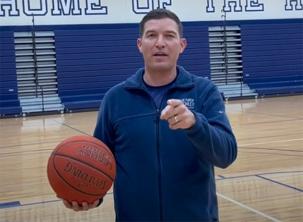 President Kavalhuna on a basketball court, holding a ball and pointing at the camera
