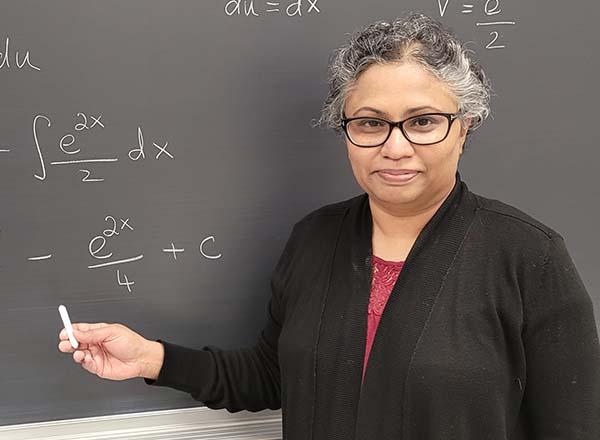 Dr. Rama Chidambaram in front of a blackboard. 
