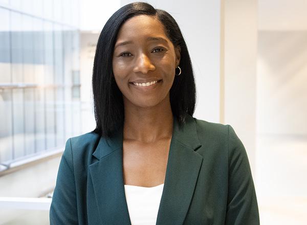 Headshot of DeJanae Hayes, who has dark shoulder length hair and is wearing a navy business jacket. 