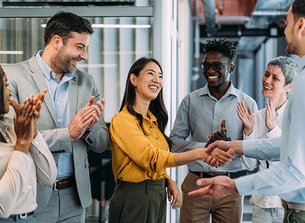 Business people shaking hands and clapping for fellow employee in the office.