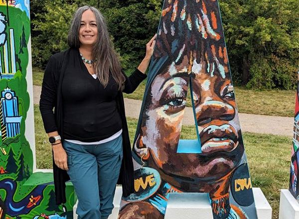 Artist Teresa Dunn standing next to a painted sculpture of the letter A.