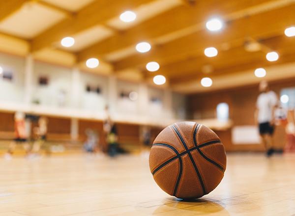 Basketball on Wooden Court Floor Close Up with Blurred Players 