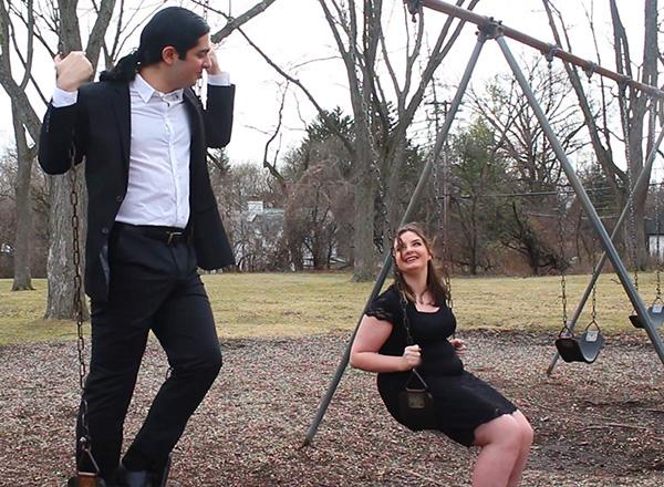 Man standing on top of swing looking down at woman sitting on a swing in a park.