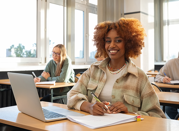Smiling student in classroom working on laptop.