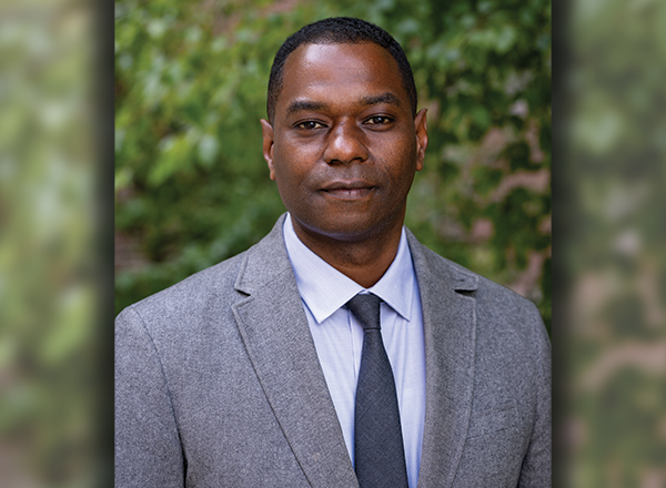 Dr. Jason Young's headshot, wearing a light grey suit and tie, a green nature background.