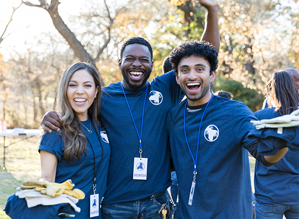 Diverse friends smile cheerfully at the camera while volunteering together to cleanup their community.