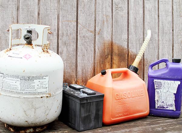 Household hazardous waste products. Gasoline container, propane gas cylinder tank, battery, and plastic chemical solvent container.