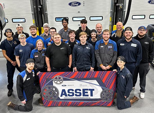 ASSET class with instructor Kris Young holding ASSET sign in automotive garage.