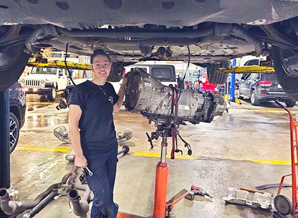 Georgia Travis standing underneath of a car working on it. 