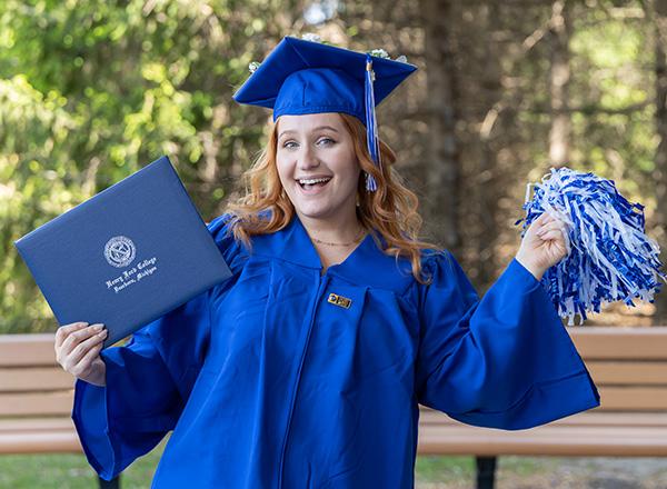 HFC grad celebrating with pom pom and holding diploma.