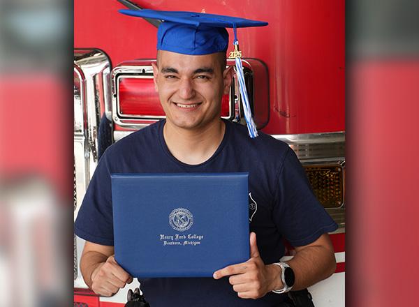  Kenneth Lee Isaacson holds up his diploma while wearing his graduation cap and sitting in front of a fire engine.