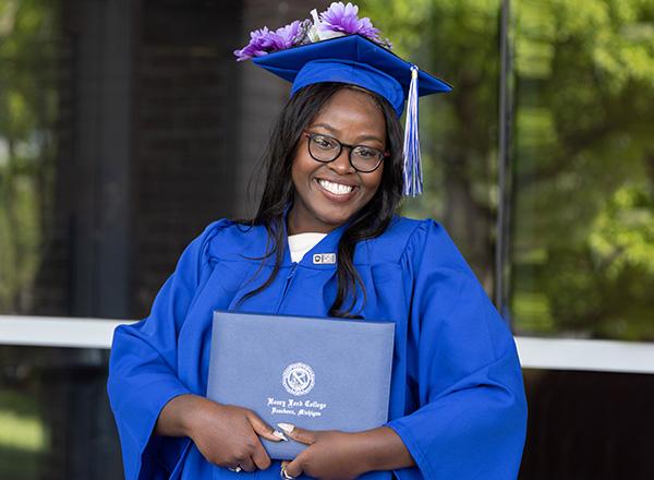 A female HFC graduate in cap and gown holding her diploma. 