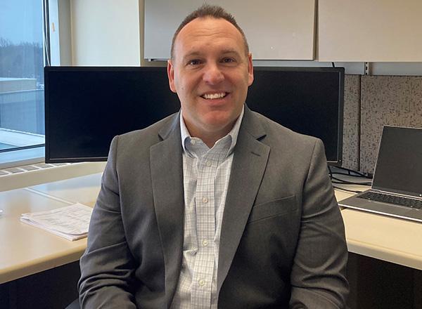 Michael Takach is sitting at his desk, smiling.