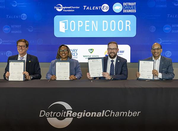 Four people sitting at a table holding up documents they have signed.