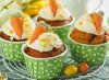 Four carrot cake cupcakes wrapped in green and white polka dot wrappers topped with white frosting and a frosted faux carrot. 